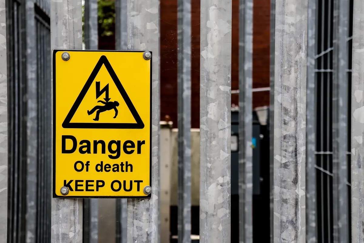 Close-up of a danger of death warning sign on a metal fence outdoors.