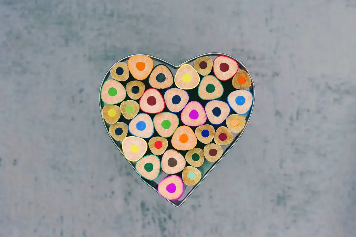 Color pencils arranged in a heart shape on a textured gray background, showcasing various vibrant hues.