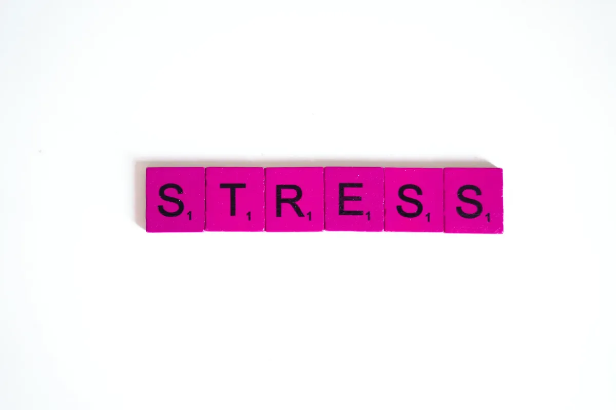 Pink Scrabble tiles spelling 'stress' arranged on a clean white background, emphasizing mental health.
