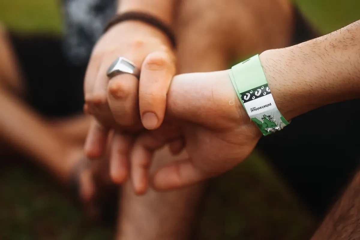 A detailed close-up of two hands clasped together, featuring a wristband, outdoors.