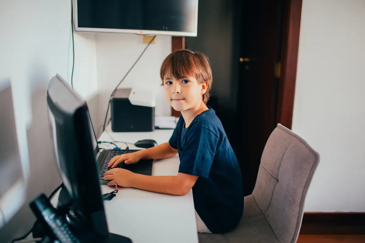 Boy in a home office setting focused on using a computer. Modern technology and learning concept.