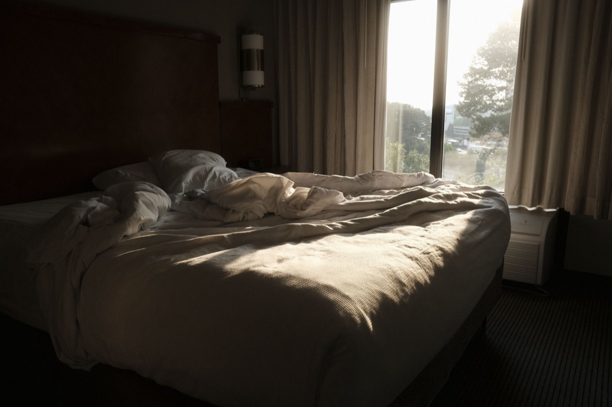 Sunlight hitting rumpled white bed sheets in a bright bedroom.