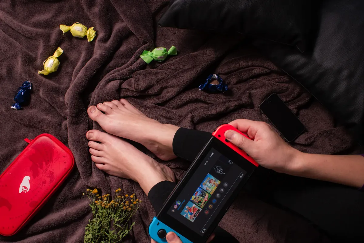Close-up of a person playing Nintendo Switch with candy and a cozy blanket.