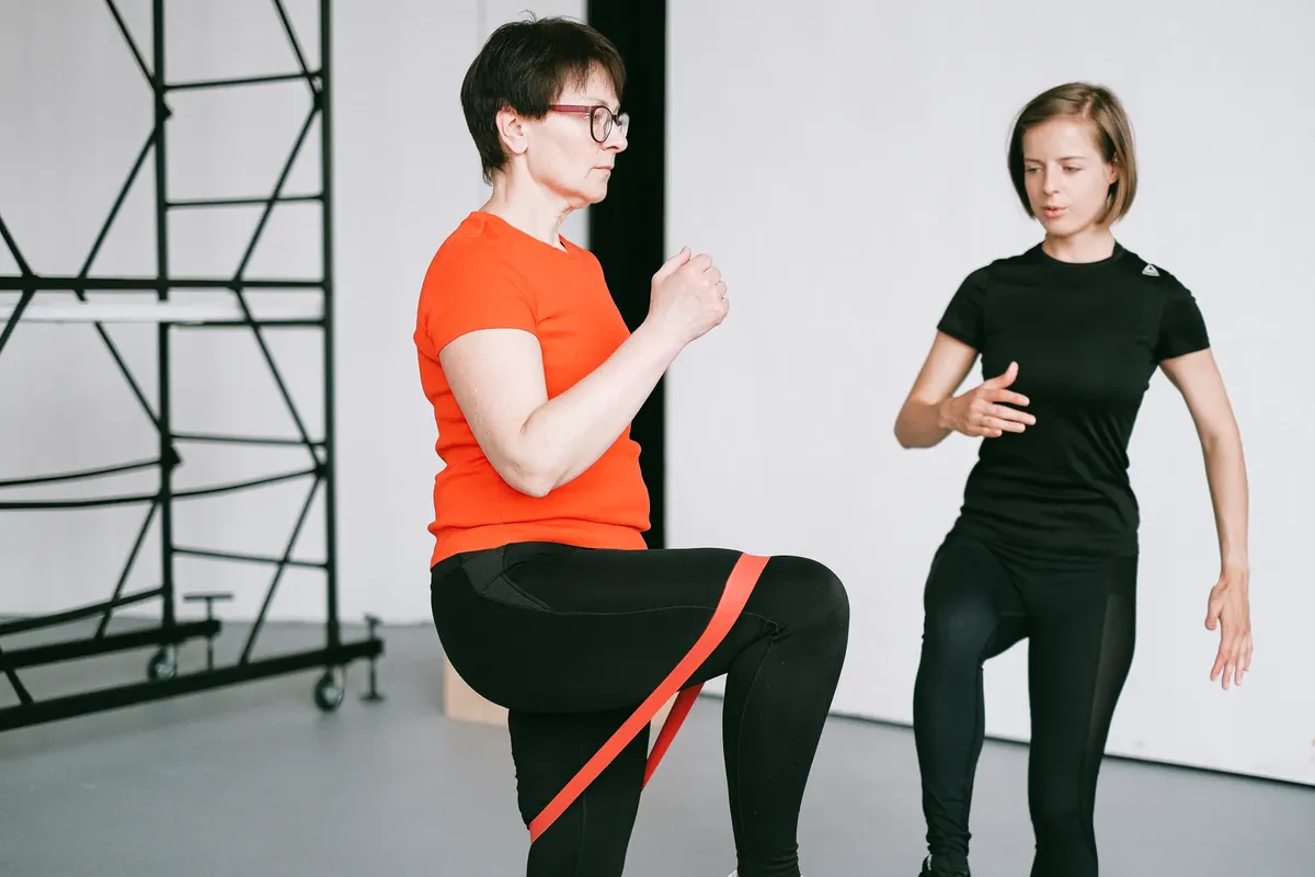 Personal trainer guiding a woman with resistance band exercise in a gym setting.