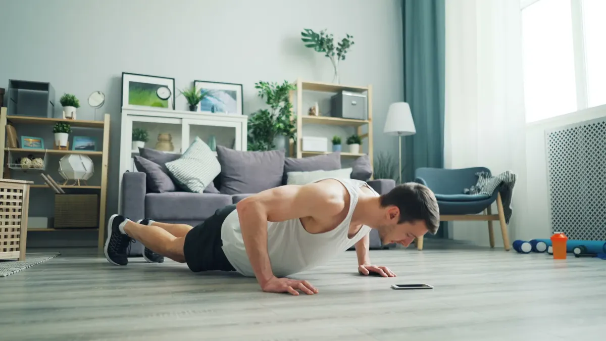 A muscular man performing push-ups in a modern living room, showcasing home fitness.